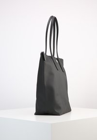 Borsa tote nera con finitura testurizzata, dotata di due manici lunghi, chiusura con zip e design minimalista. Esterno liscio senza accenti aggiuntivi.