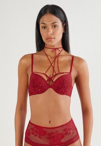 Red lace bra with underwire and decorative crisscross detailing. Paired with matching high-waisted sheer brief featuring floral patterns.