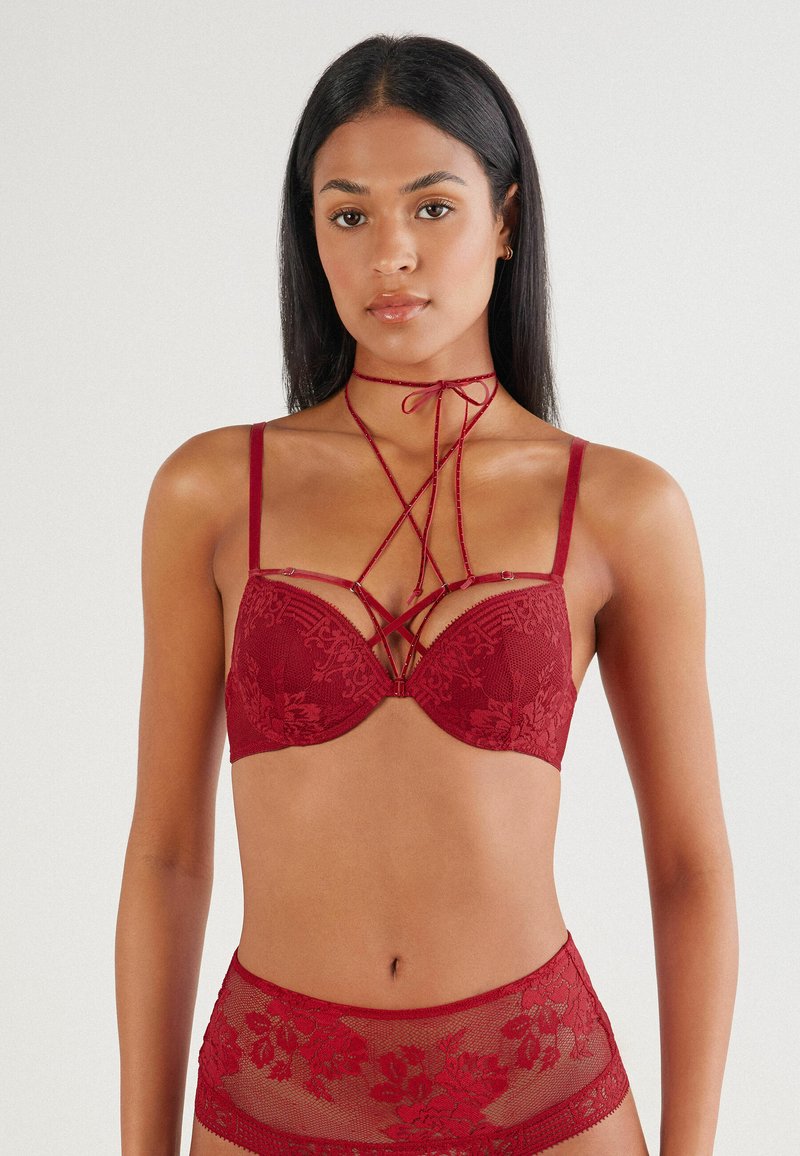 Red lace bra with underwire and decorative crisscross detailing. Paired with matching high-waisted sheer brief featuring floral patterns.