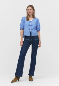 Ljusblå, kortärmad randig blus med V-hals och framknytning, som är tillsammans med mörkblå utsvängda jeans och bruna mocka klackstövlar.