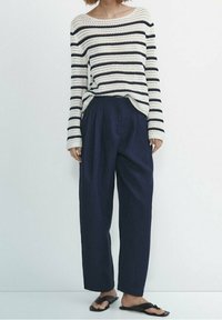 Gebreide gestreepte trui in crème en marineblauw; loszittende marineblauwe broek; zwarte platte sandalen met twee bandjes; casual outfit met een ontspannen silhouet.