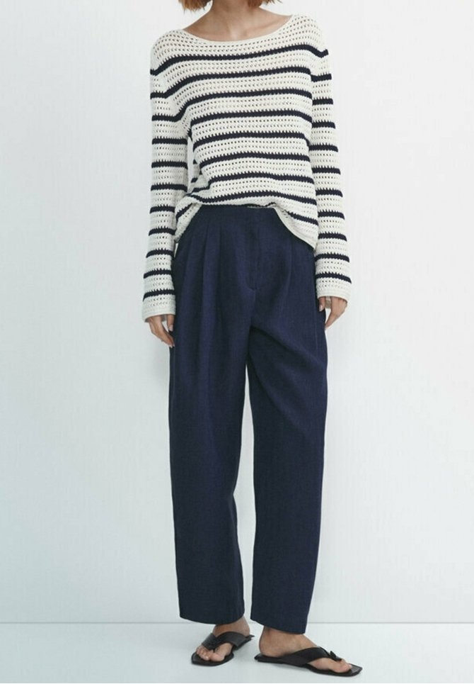 Gebreide gestreepte trui in crème en marineblauw; loszittende marineblauwe broek; zwarte platte sandalen met twee bandjes; casual outfit met een ontspannen silhouet.