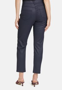 Marineblaue, enganliegende Hose mit glatter Textur, vier Taschen und geradem Bein. Getragen mit offenen, absatzhohen Schuhen.