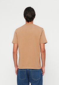 T-shirt beige à manches courtes en coton, avec un col rond et une coupe regular, présenté de dos avec une texture uni.