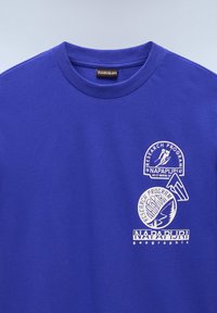 Purple crew neck t-shirt made of cotton, featuring white graphic prints of logos and icons related to research programs. Smooth texture.