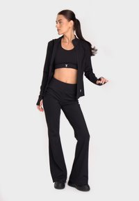 Črna aktivna športna obleka, ki vključuje prilegajoč se kratki top, usklajene raztegne hlače in zadrgo jakno. Gladka tekstura z naglasom logotipa.