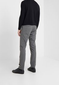 Grijze broeken van stof met een gladde textuur, voorzien van een getailleerde pasvorm en zijzakken, gecombineerd met zwarte schoenen en een gebreide zwarte trui.
