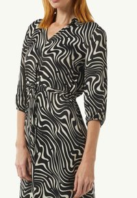 Czarna i kremowa sukienka w kręcącym się wzorze, z dekoltem w serek i rękawami o długości 3/4, zszyta w talii z detalem w postaci wiązania.