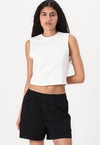 Bílý bezrukávový crop top a černé šortky s výšivkou broderie anglaise. Tento outfit má volný střih a elastický pas.