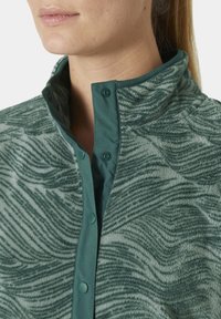 Veste en polaire verte avec un motif en vagues texturé, fermeture à boutons-pression et un col lisse contrastant d'une teinte verte plus foncée.