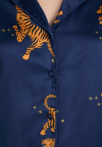 Blå satinskjorte med oransje tigermønster og stjernemønstre, med krage og en enkel knapp foran.