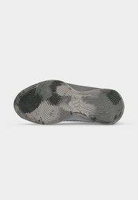 Semelle usée grise et noire à motif d'une chaussure de sport unique vue de dessous sur fond blanc.