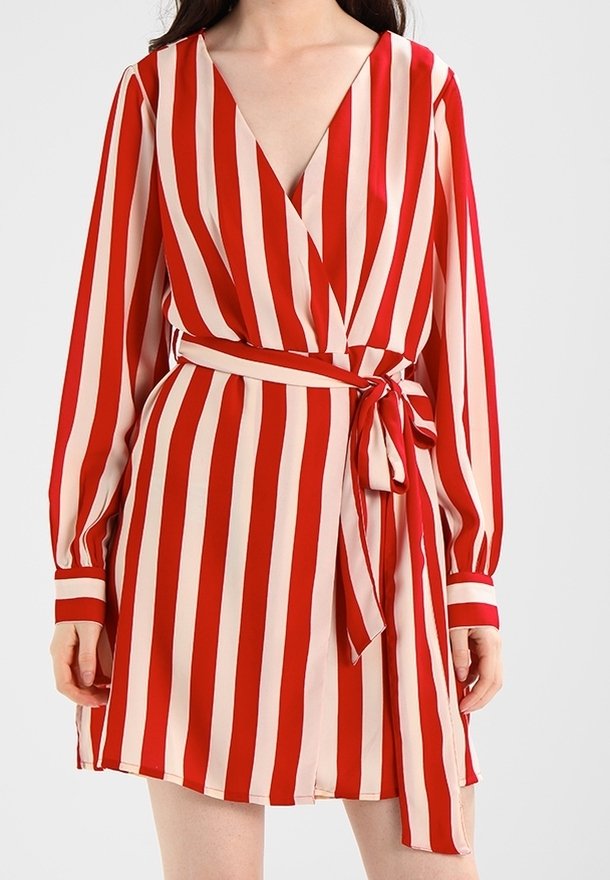 Femme portant une robe portefeuille à rayures verticales rouges et rose clair, manches longues et ceinture nouée à la taille.