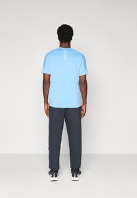 Lysblå kortærmet t-shirt med en lige nederkant og teksturerede detaljer, parret med mørkegrå sweatpants og sorte sneakers.