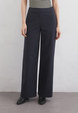 Pantaloni largi bleumarin, dintr-un amestec de bumbac, cu talie înaltă și buzunare frontale, asortați cu cizme negre cu vârful ascuțit.