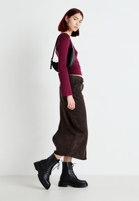 Sorte snørebukser i kampsko med kraftige såler, brukt med en maroon langermet topp og brun denimskjørt, kombinert med en liten svart skulderveske.