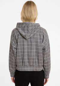 Veste à capuche grise avec un motif à carreaux, fabriquée dans un tissu doux. Caractéristiques : ourlet et poignets élastiques, offrant une coupe décontractée dans un design court.