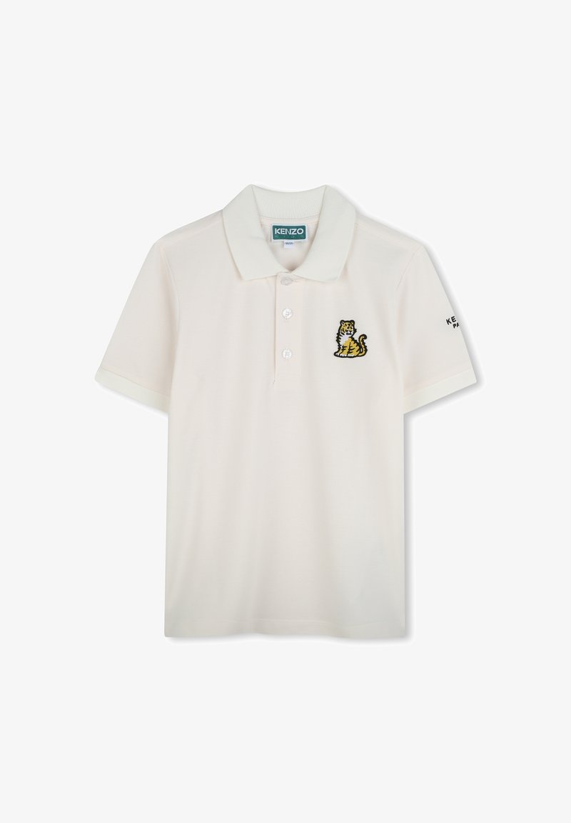 Polo en coton beige clair avec un col, trois boutons et un logo brodé de tigre sur la poitrine gauche. Manches courtes.