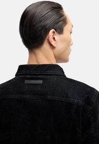 Czarna kurtka dżinsowa o fakturowanym wykończeniu, z klasycznym kołnierzem, karczkiem na plecach oraz metką marki umieszczoną nad szwem z tyłu.