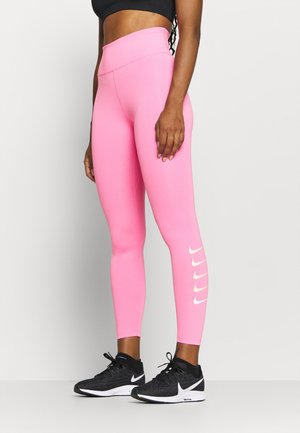 Vaaleanpunaiset urheilulegginsit, joissa on korkea vyötärö ja tiukka muotoilu. Alhaalla on valkoisia Nike-logoja. Yhdistetty mustiin lenkkareihin.