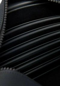 Interno di una borsa in pelle nera con texture rigata, caratterizzata da lati lisci e una cerniera a contrasto. Messa a fuoco sul design della fodera strutturata.