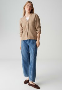 Cardigan beige con scollo a V e tre bottoni, abbinato a jeans a vita alta azzurri e ballerine marrone scuro. Tessuto liscio e vestibilità casual.