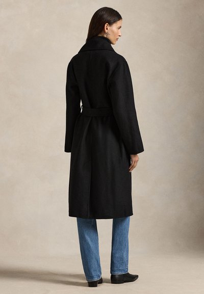Černý kabát z vlněné směsi s vysokým límcem, opaskem v pase a dlouhými rukávy. V kombinaci s modrými džíny a černými kotníkovými botami.