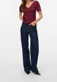 Bordeauxfarbenes, geripptes Kurzarmhemd mit Knopfleiste, kombiniert mit dunkelblauen, weit geschnittenen Jeans und schwarzen spitzen High Heels.