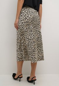 Leopardenmuster-Midikleid in Beige und Schwarz, mit einem luftigen Design und einem elastischen Bund. Kombiniert mit schwarzen Absatzsandalen.