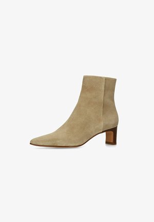 Beige suède enkellaars met puntige neus en lage blokhak in bruin, weergegeven vanaf de rechterkant op een witte achtergrond.