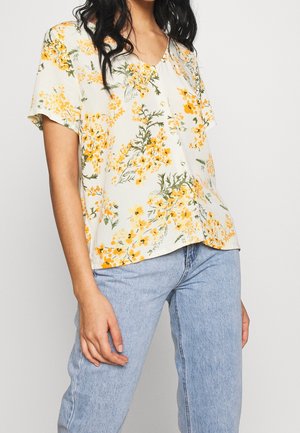 Blusa floreale a maniche corte realizzata in tessuto leggero, con scollatura a V decorata con fiori gialli e foglie verdi su uno sfondo crema.