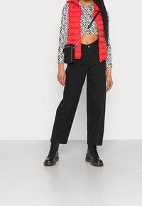 Rote Weste, schwarz-weiß gestreiftes, kurz geschnittenes Oberteil, schwarze weite Hose und schwarze Schnürstiefel. Schwarze Umhängetasche inklusive.