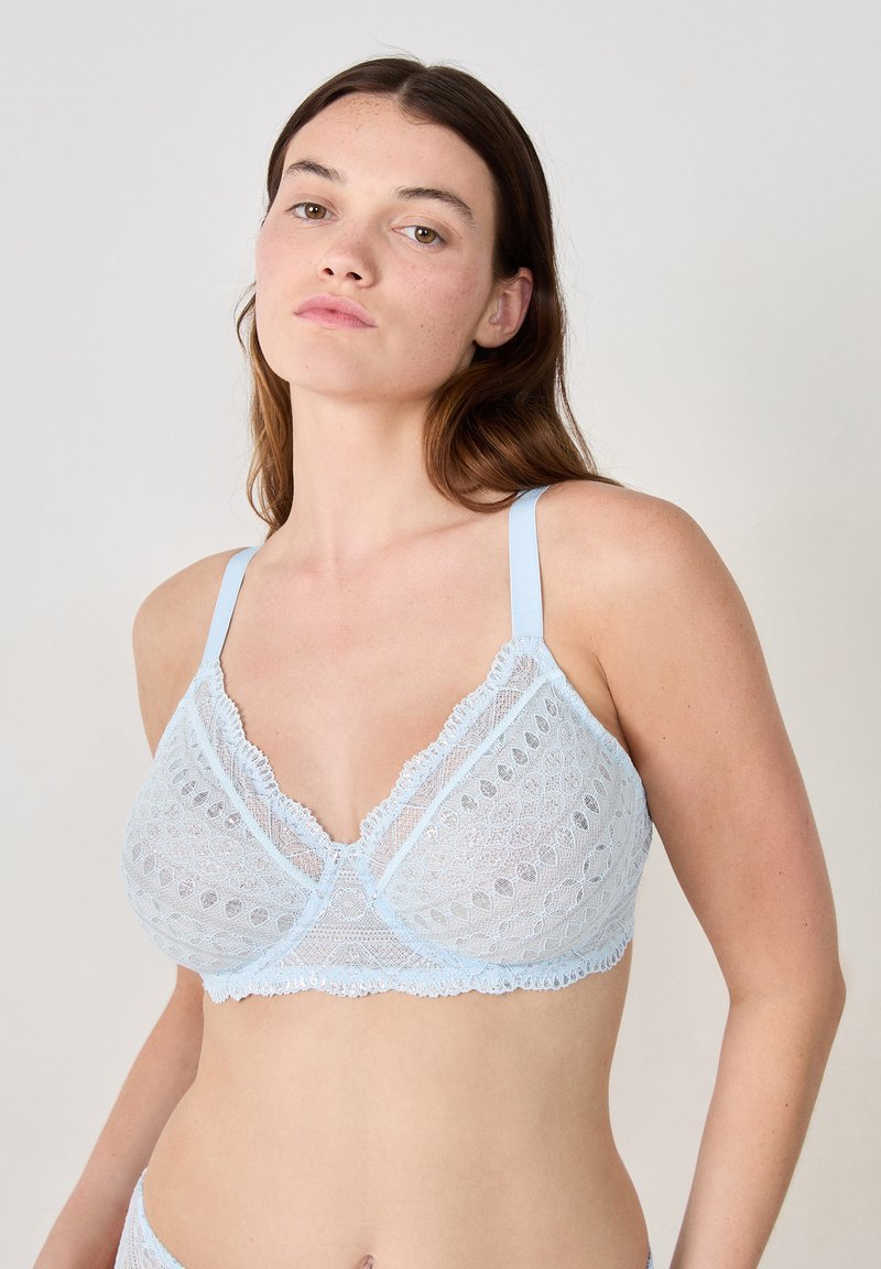 Bralette en dentelle bleu clair avec des motifs circulaires complexes, des bords en festons et des bretelles réglables. Texture douce et transparente avec une forme triangulaire.