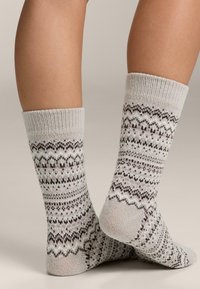 Szare wzorzyste skarpetki z dzianym wzorem naprzemiennych falistych i zygzakowatych linii, ozdobione małymi ciemnoczerwonymi kropkami.