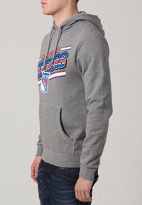 Sudadera gris con un bolsillo frontal, que presenta un colorido texto y logotipo de "New York Rangers", hecha de una tela suave y con un corte relajado.