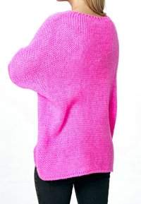 Růžový pletený svetr s volným, oversized střihem. Má žebrovaný výstřih a texturovanou látku, kombinovaný s tmavými džíny.