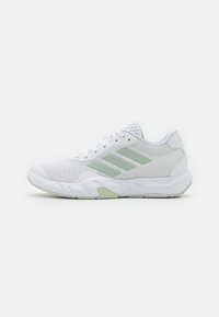 White athletic shoe with mesh upper, green accents, and textured sole. Features white laces and three logo stripes on the side.