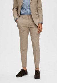 Beige taillored broek gemaakt van een gestructureerde stof, met een slim fit. Gemonteerd met een lichtblauw shirt en bruine suède schoenen.