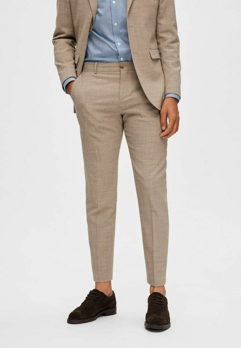 Beige taillored broek gemaakt van een gestructureerde stof, met een slim fit. Gemonteerd met een lichtblauw shirt en bruine suède schoenen.