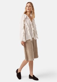 Lichtgewicht, witte blouse met ruches en een diepe V-hals, gecombineerd met beige wijde shorts en zwarte suède loafers. Soepel, gestructureerd ontwerp.