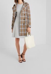 Brun rutigt ytterplagg med dubbelknapprad, grå ribbad klänning, krämfärgad axelväska och bruna remsandaler med klack.