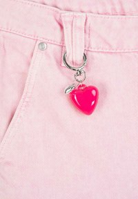 Różowa tkanina dżinsowa z metalową pętlą w kolorze srebrnym, która ma sercowy różowy charms i mały detal w kształcie liścia.