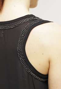 Haut noir sans manches en tissu fin texturé avec des détails décoratifs en perles le long de l'encolure et des coutures des épaules.