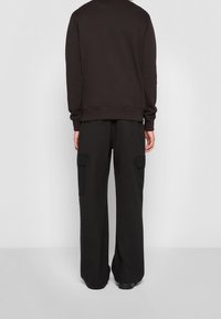 Černá mikina s žebrovanými manžetami a lemem v kombinaci s černými širokými kalhotami typu cargo s bočními kapsami a hladkým povrchem.