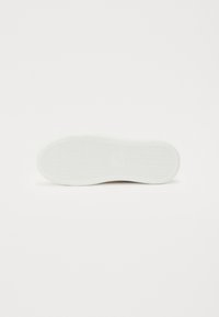 White sneaker sole, rubber material, textured grip pattern, rounded shape, and subtle branding impression on the surface.