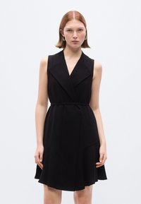 Μαύρο αμάνικο φόρε μα με V-λαιμόκοψη, φαρδιές πέτο, ζώνη στη μέση και φουσκωτό τελείωμα. Κατασκευασμένο από λείο ύφασμα με μίνιμαλ σχεδιασμό.