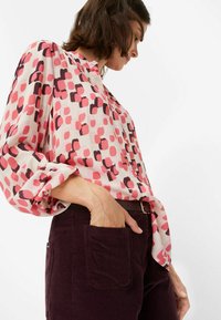 Blouse à manches longues crème avec un motif abstrait rose et bordeaux ; tissu léger ; portée avec un pantalon en velours côtelé violet foncé.
