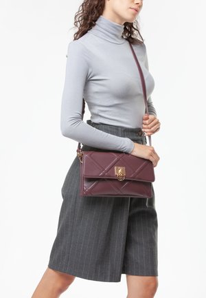 Bolso de mano acolchado burdeos de piel con herrajes dorados y cierre de solapa. Presenta una correa delgada para el hombro y una forma rectangular.