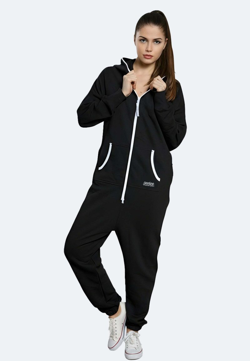 Tuta nera con zip realizzata in morbido tessuto, con accenti bianchi, tasche laterali e una vestibilità rilassata. Abbinata a sneakers bianche.