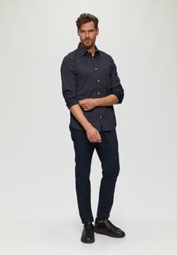 Marineblauwe button-up shirt met witte stippen, opgerolde mouwen, gecombineerd met donkere broeken en zwarte sneakers. Eenvoudig ontwerp, gladde textuur.